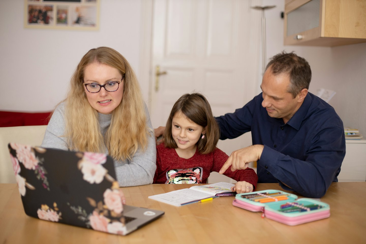 Eltern helfen Tochter bei den Hausaufgaben am Laptop.