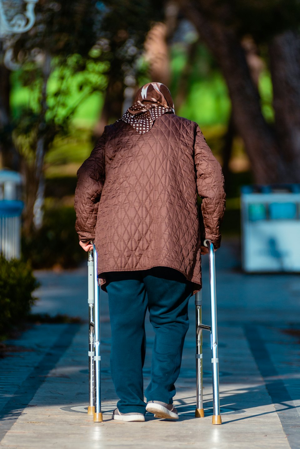Eine Person mit Gehhilfe spaziert auf einem Parkweg.