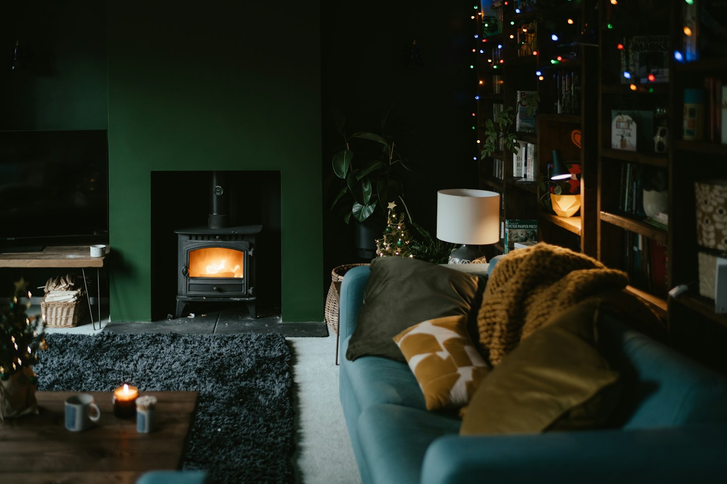 Gemütliches Wohnzimmer mit leuchtendem Kamin und türkisfarbener Couch.